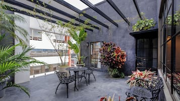 Une terrasse sur le toit, avec une table et des chaises en métal noir, entourée de plantes en pot et d’une grande plante décorative.