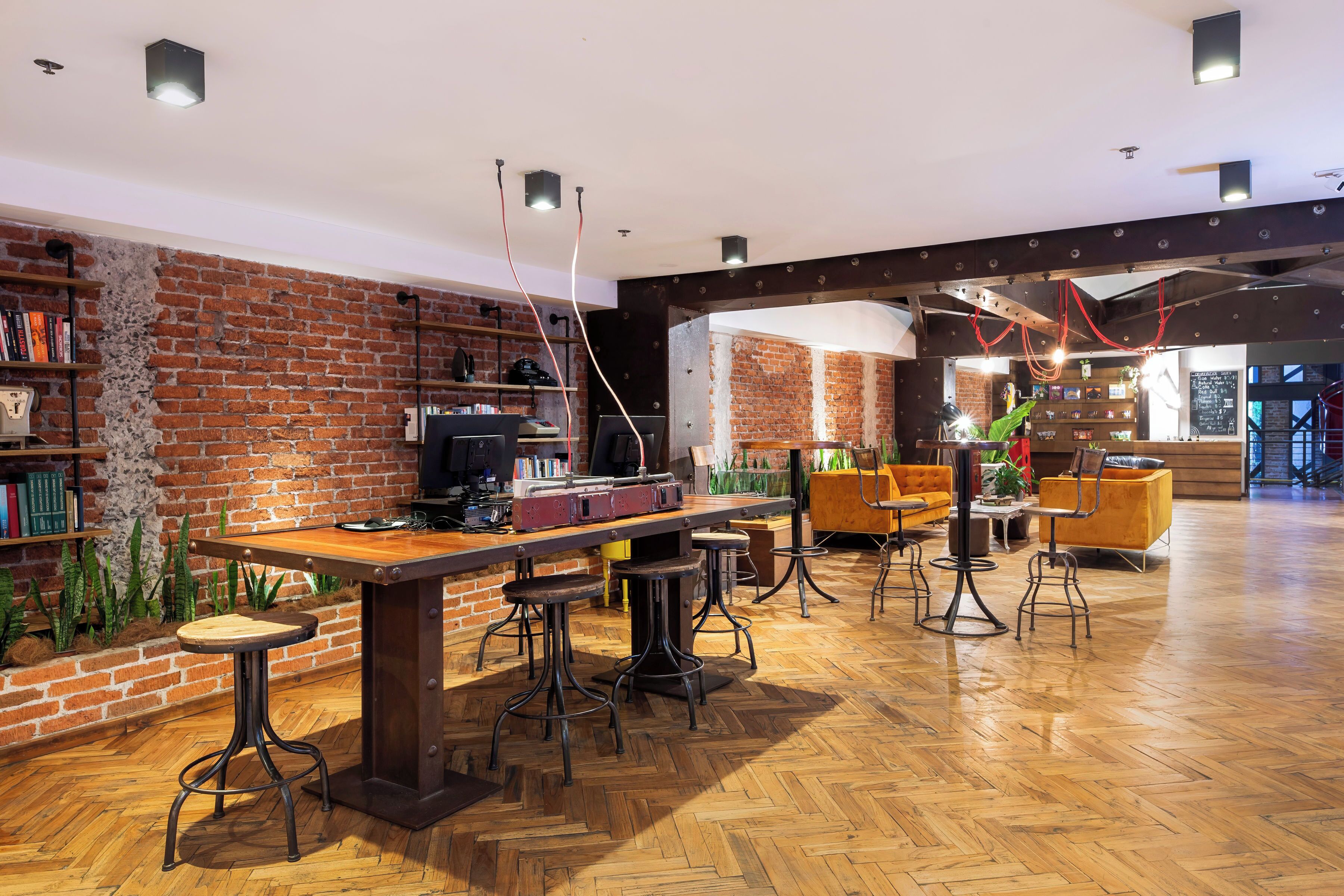 A spacious bar area with a brick wall, wooden flooring, and multiple stools.
