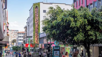 Una concurrida calle urbana con peatones, tiendas y un gran mural en un edificio.