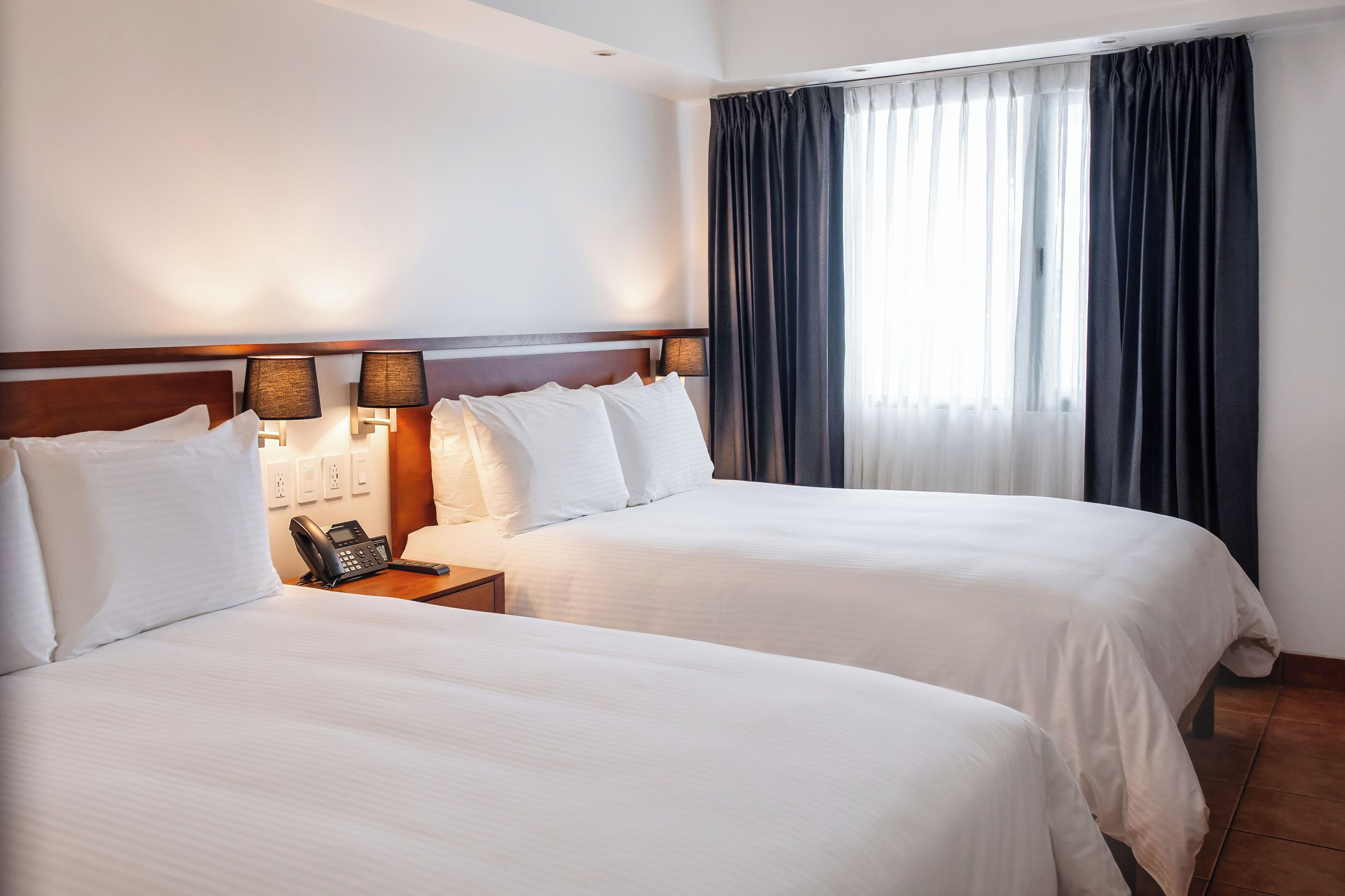 A hotel room with two beds, a bedside telephone, and a window with curtains.