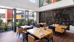 A modern restaurant with high ceilings, large windows, and a mural on the wall.