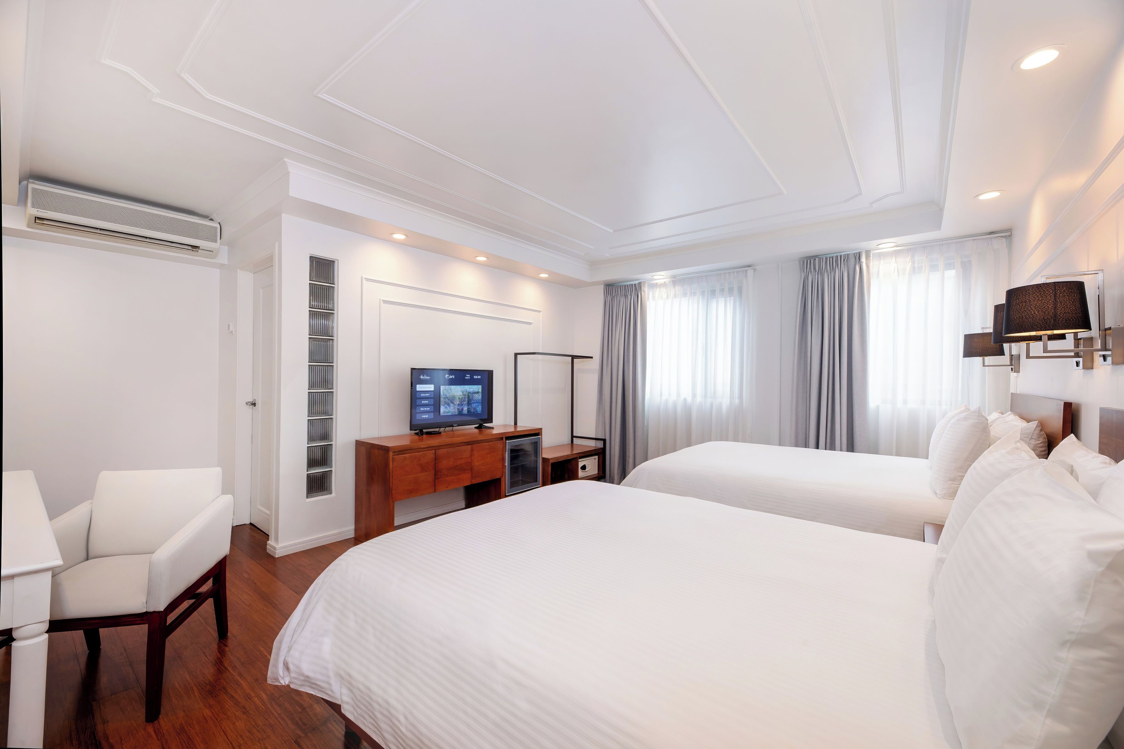 Une chambre d’hôtel avec deux lits, un bureau avec une télévision, une chaise et une armoire.