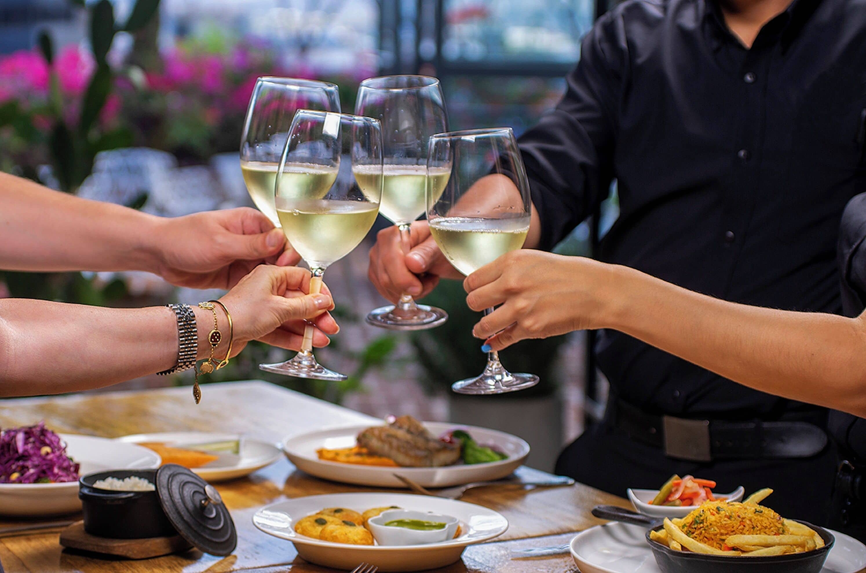 A group of people toasting with wine glasses at a table with various dishes.