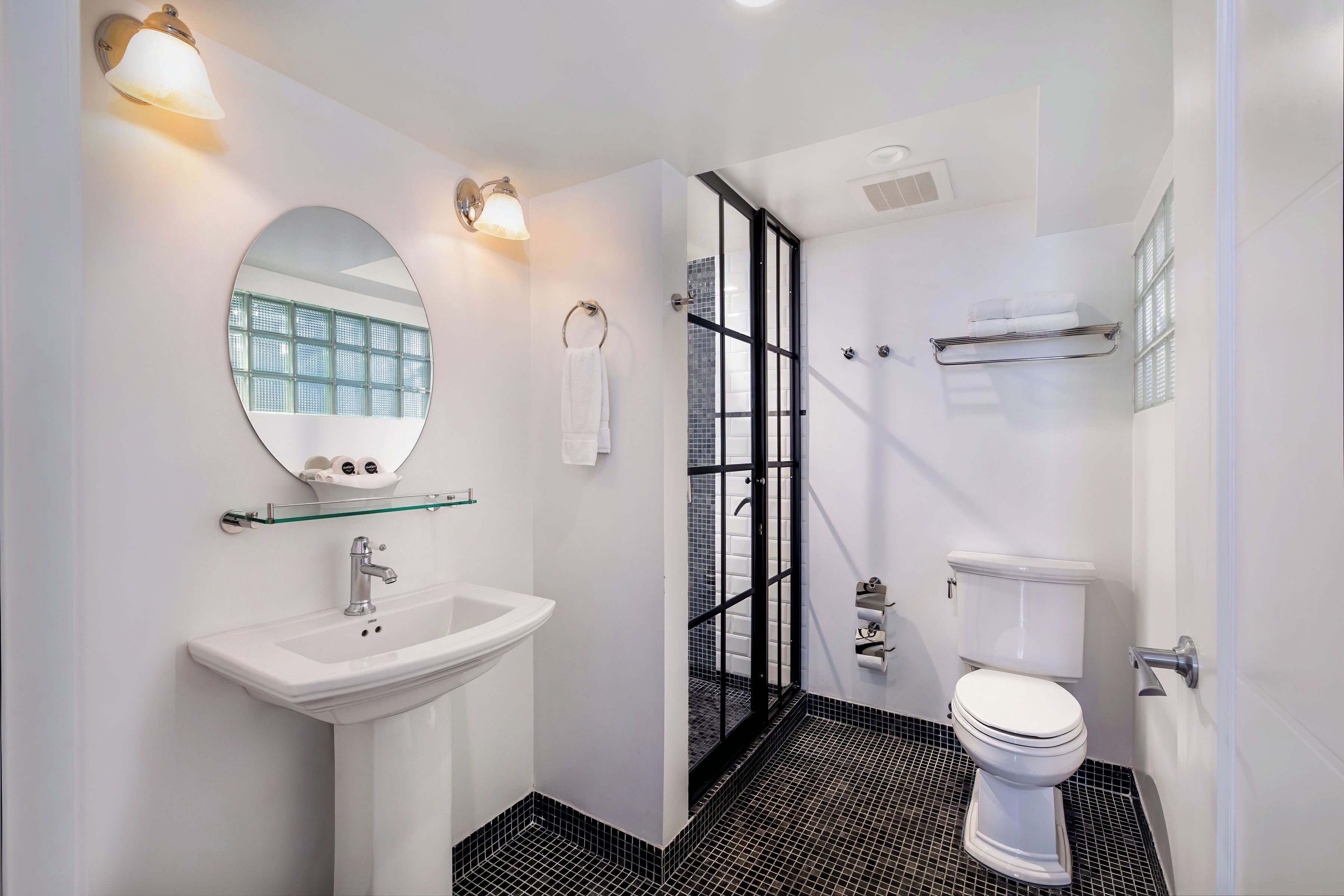 A modern bathroom with a white sink, round mirror, and black-tiled shower area.