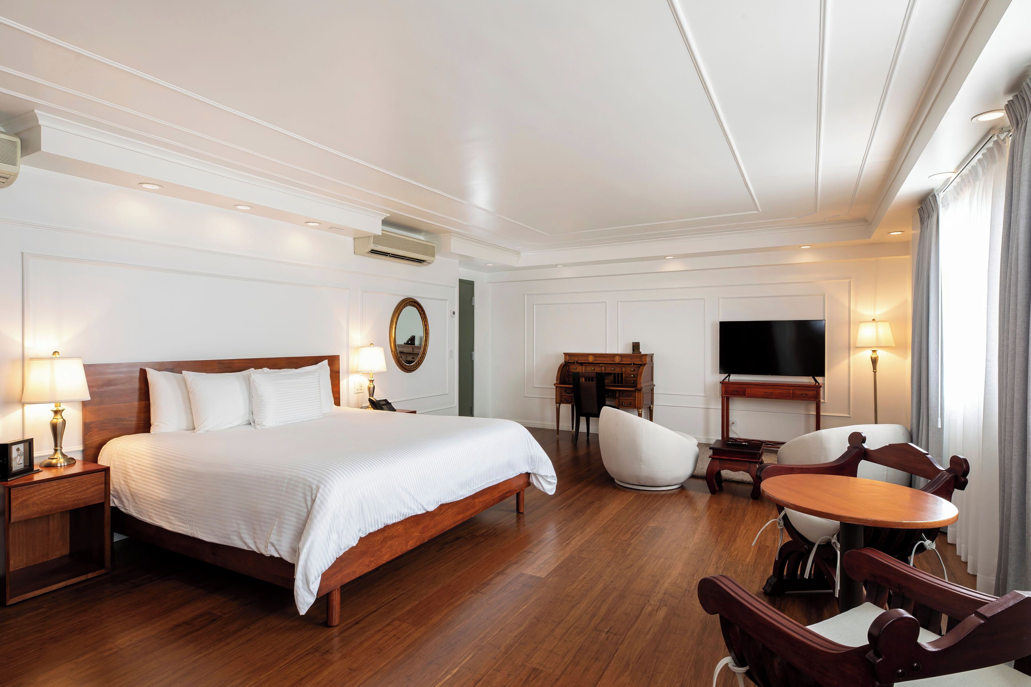 A hotel room with a large bed, wooden furniture, a desk, a chair, and a TV.