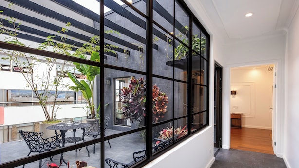 A modern interior with a large window, a balcony with outdoor seating, and a view of the cityscape.