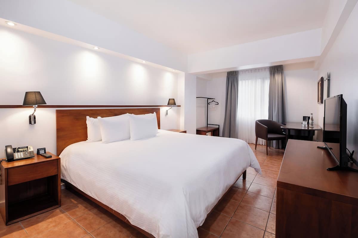 A hotel room with a large bed, bedside tables with lamps, a desk with a chair, and a TV.