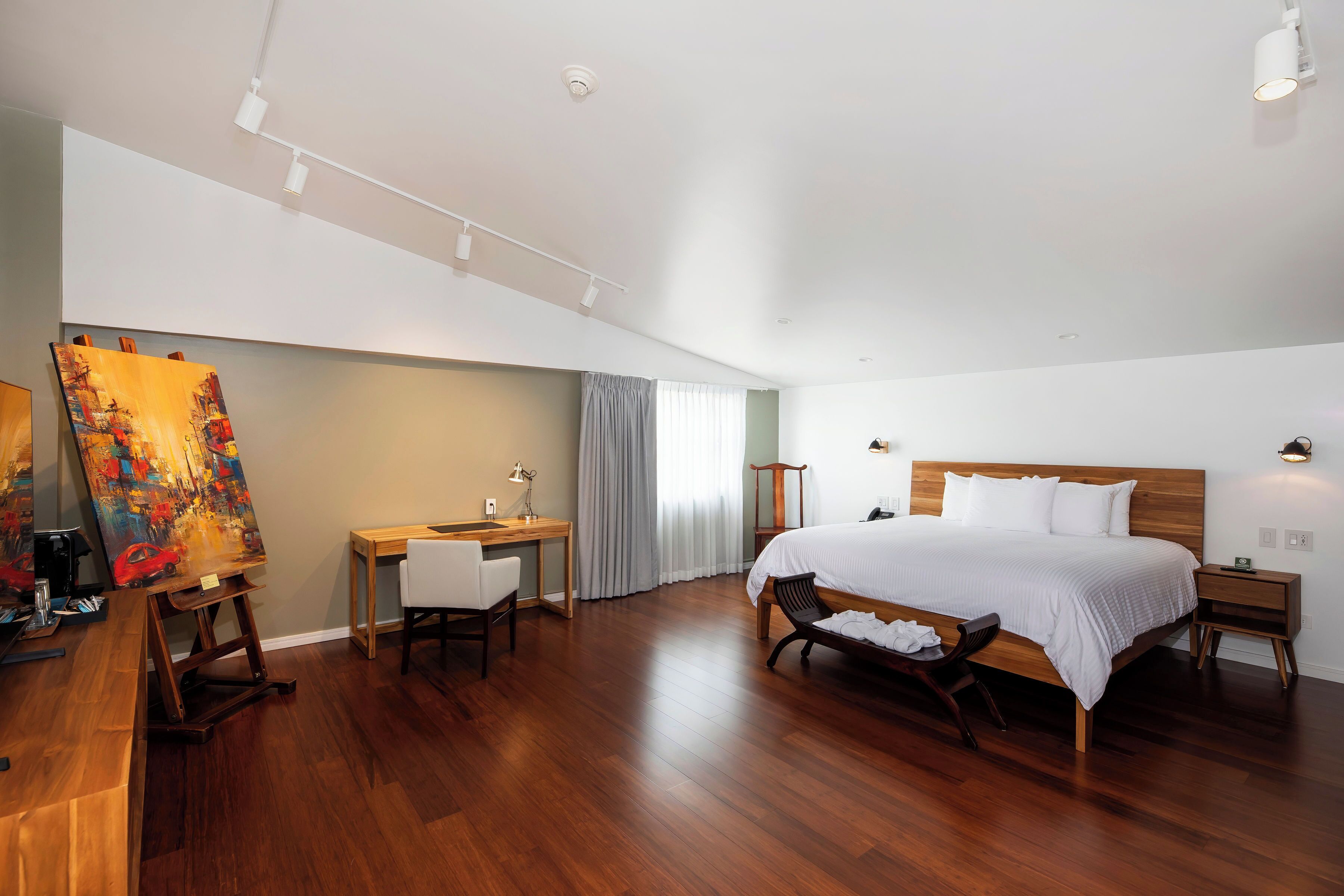 A spacious bedroom with a large bed, a desk, and an easel with a painting.