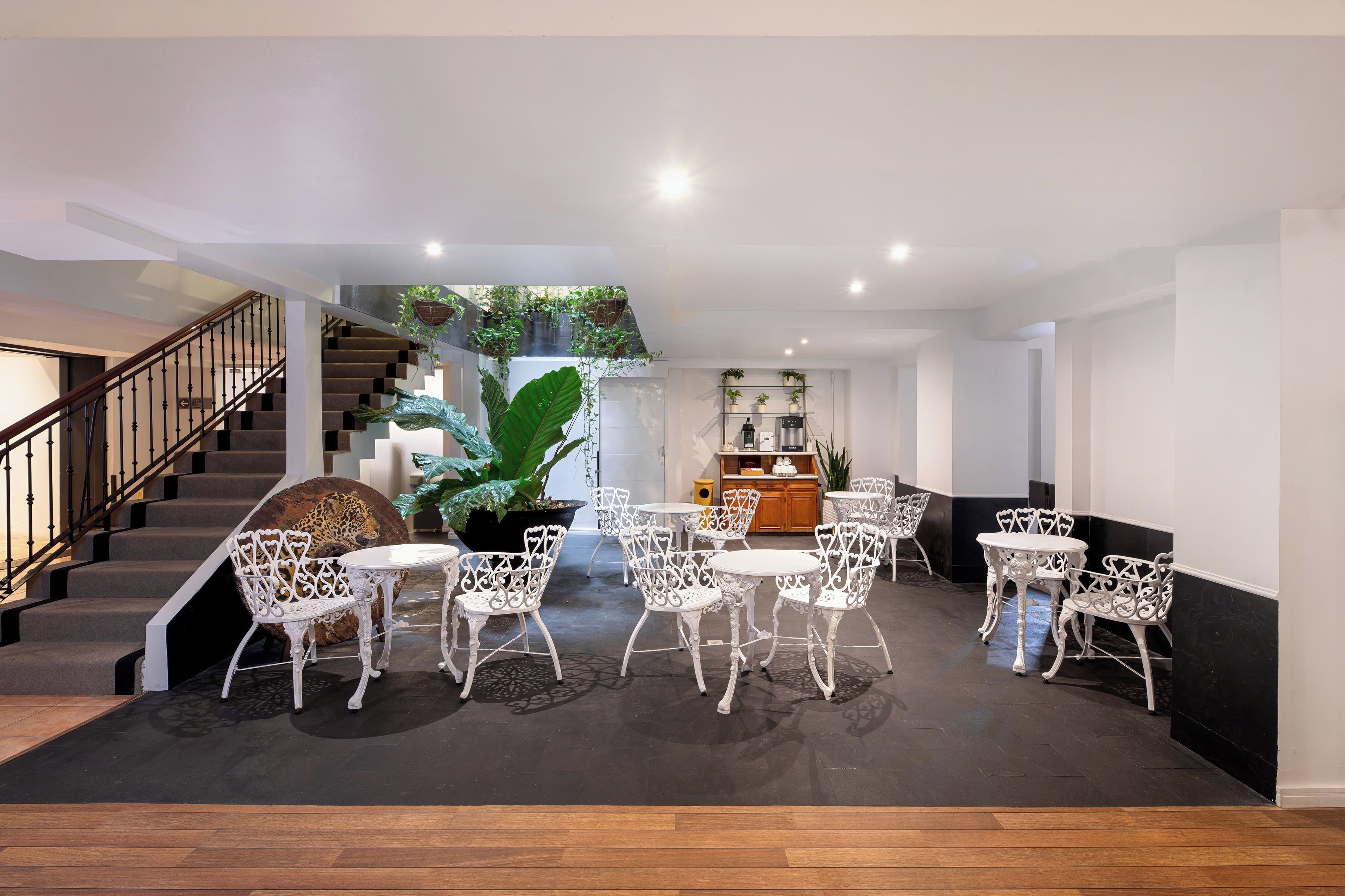 Amplio espacio interior con escalera, sillas metálicas blancas y mesas dispuestas alrededor de una planta central.