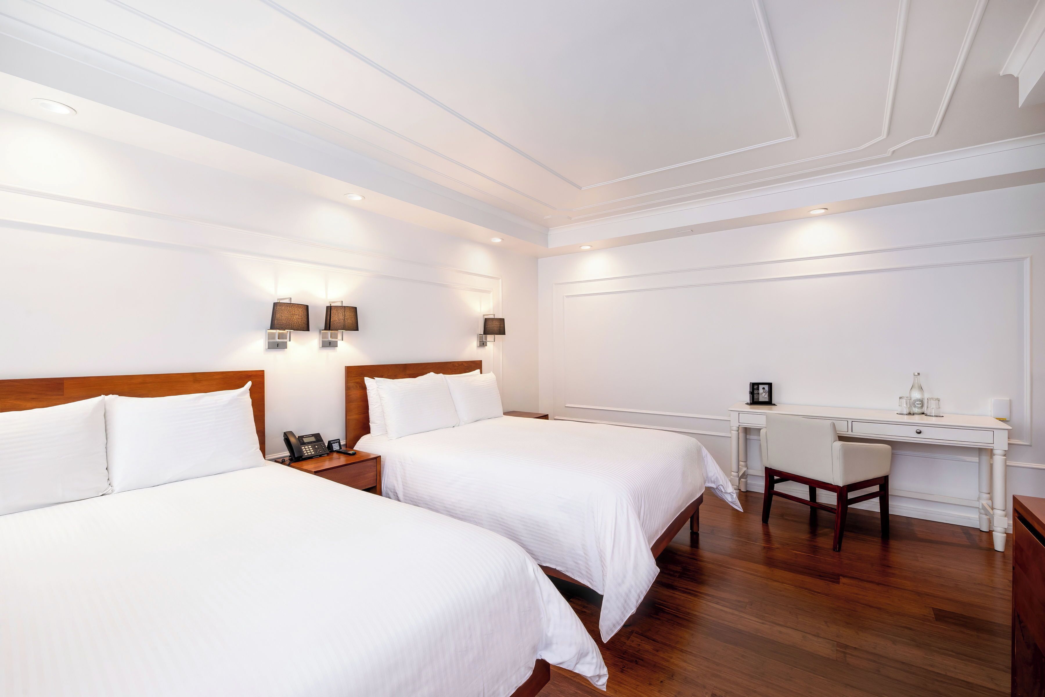 A hotel room with two beds, a desk, and a chair.