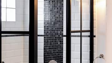 Um banheiro moderno com chuveiro em box de vidro, paredes revestidas de azulejos brancos e um painel de mosaico preto.