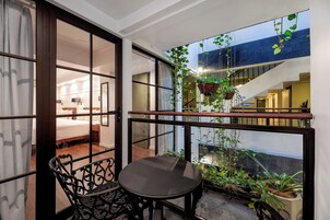Un balcón con una mesa y sillas, vista a un dormitorio y plantas colgantes.