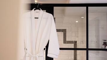A white robe hanging on a hanger in a modern bathroom with a tiled shower area visible through a glass door.