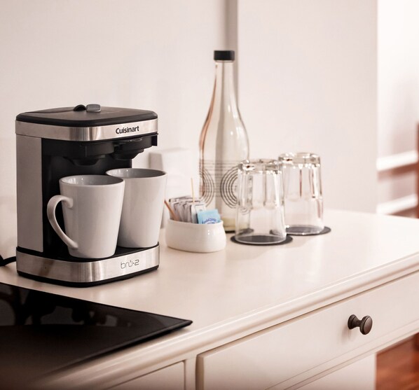 Una cafetera sobre una encimera blanca, con dos tazas blancas y una jarra de vidrio.
