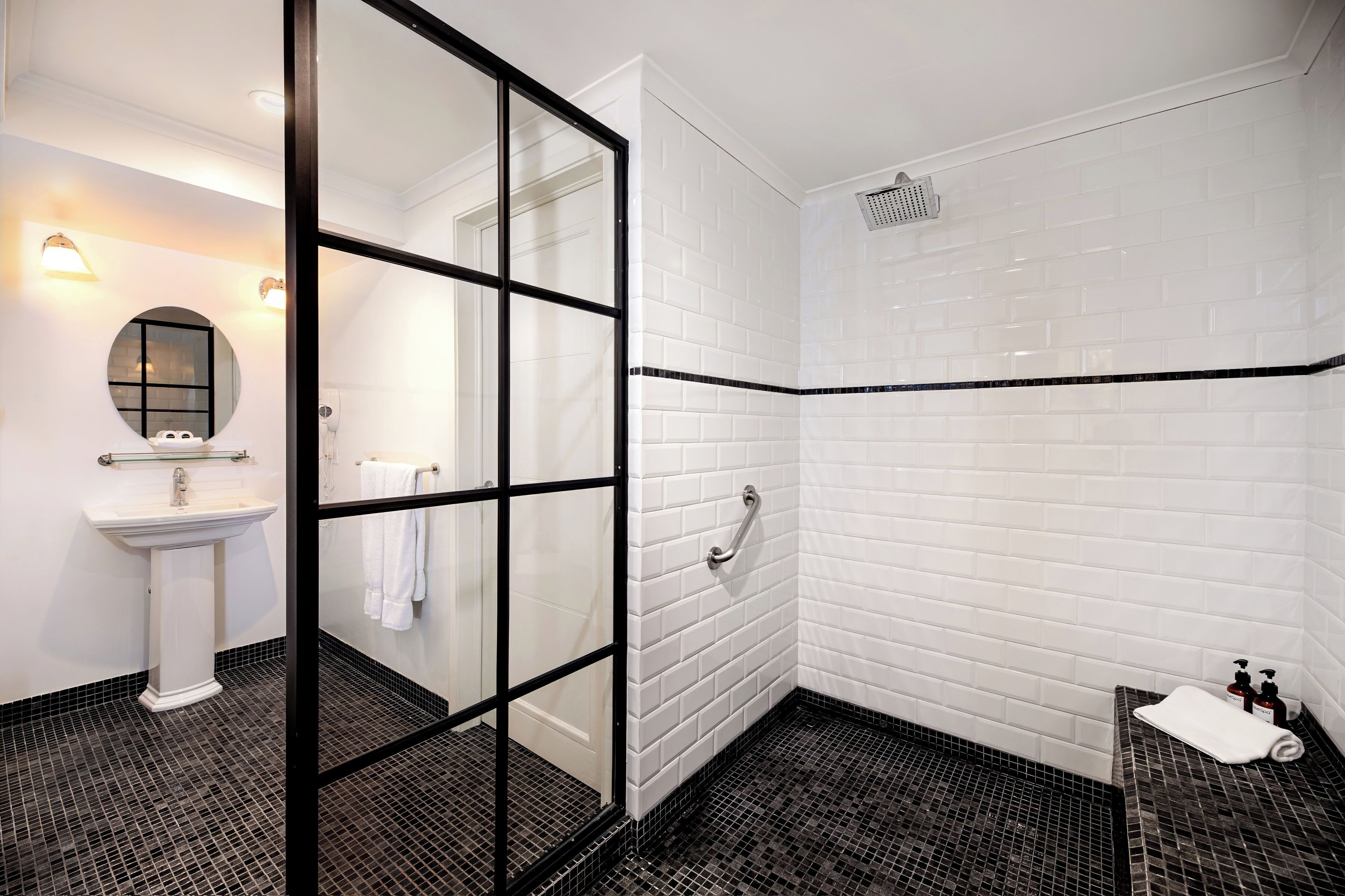 A modern bathroom with a glass shower enclosure, a white sink, and a black-tiled floor.