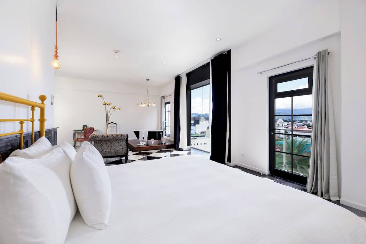 A modern hotel room with a large bed, a desk, and a view of the city.