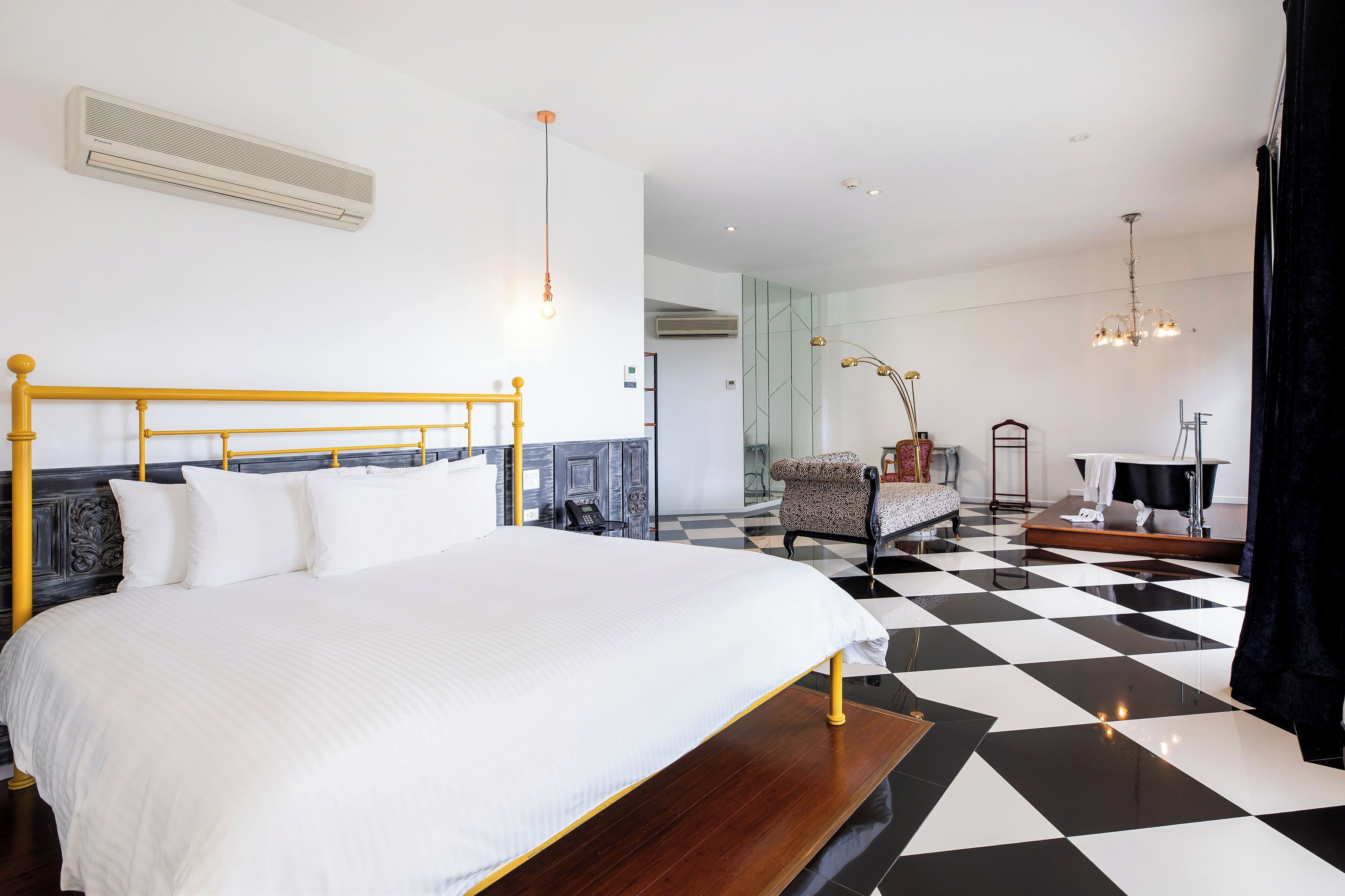 Ein modernes Hotelzimmer mit einem großen Bett, einem Schachbrettmuster-Boden, einem Schminktisch mit Spiegel und einem Sessel.
