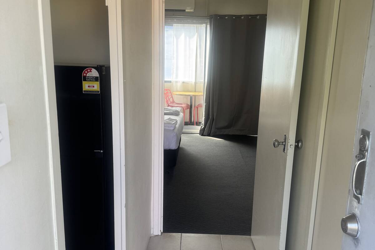A hallway with a door leading to a room with a bed, a small table, and a chair. There is a sign on the door indicating energy efficiency.