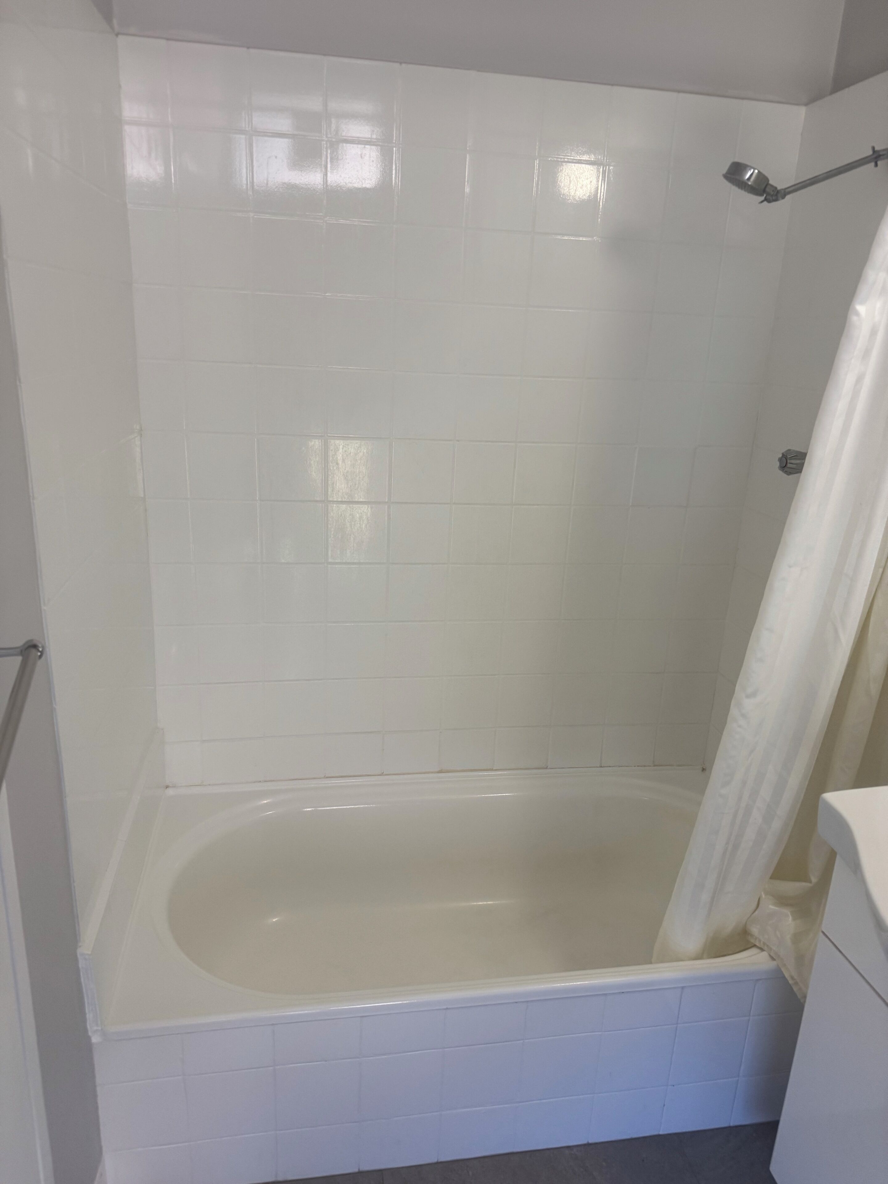 A bathroom with a bathtub, white tiled walls, and a shower curtain.