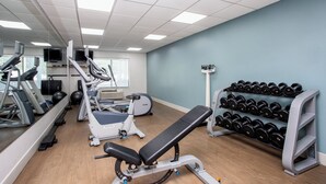 Une salle de sport équipée de machines de cardio, d’un banc et d’un porte-haltères.