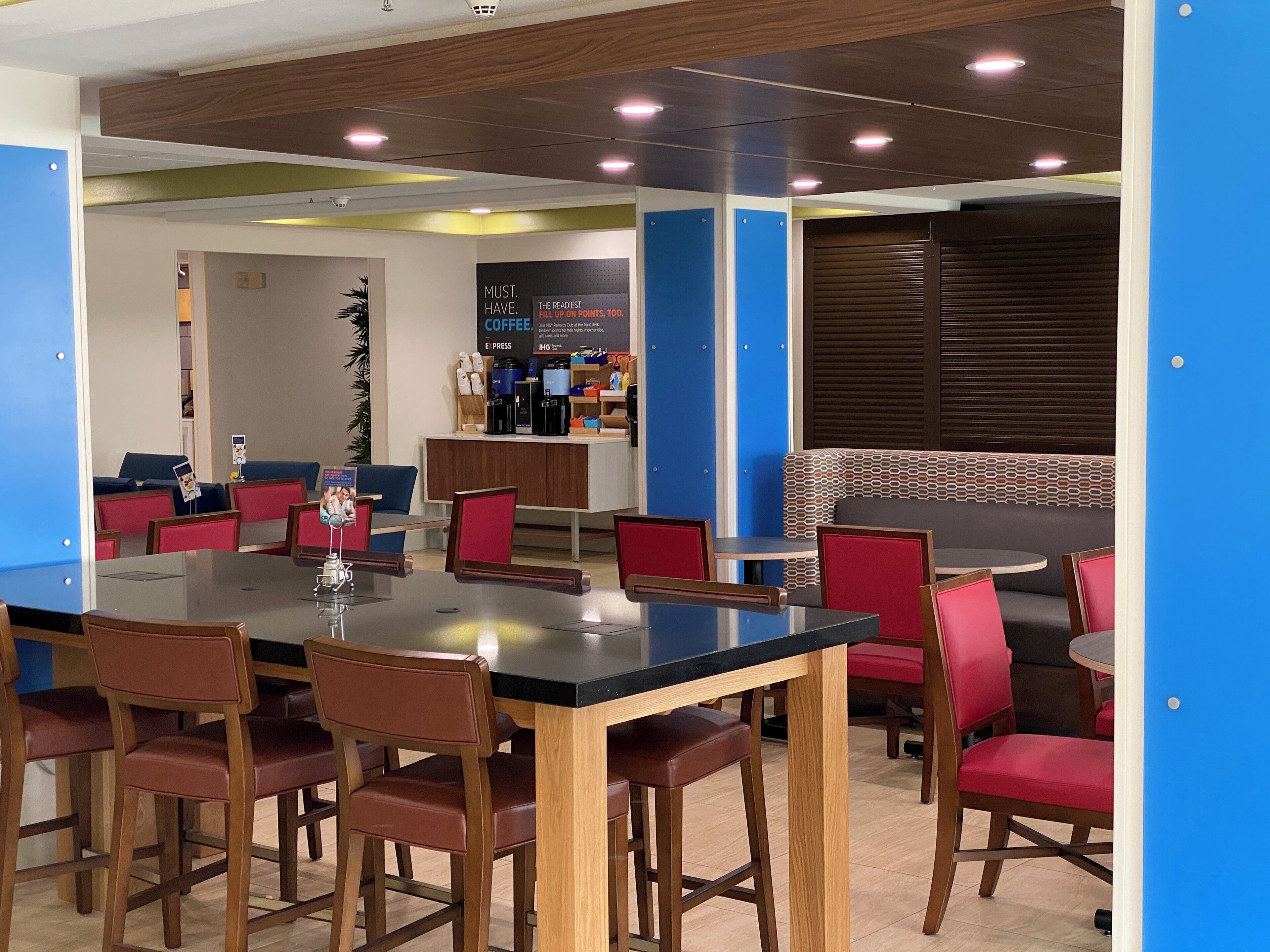 Un área de estar interior moderna con una mesa larga y varias sillas, una estación de café y una pared decorada con un diseño.