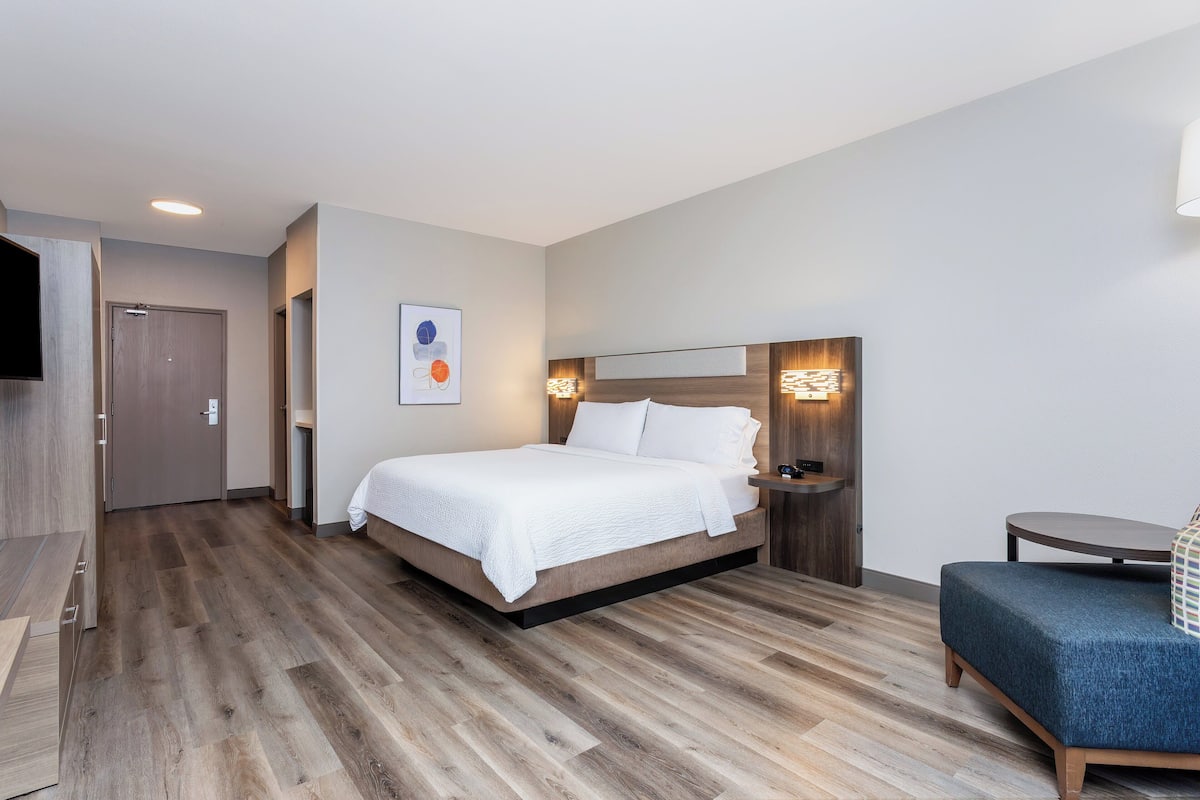 Ein modernes Hotelzimmer mit Holzboden, einem Bett mit weißer Bettwäsche, einem Nachttisch, einem kleinen runden Tisch und einem blauen Sofa.