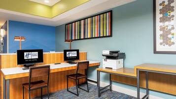 A hotel reception desk with two monitors, a printer, and a framed artwork on the wall.
