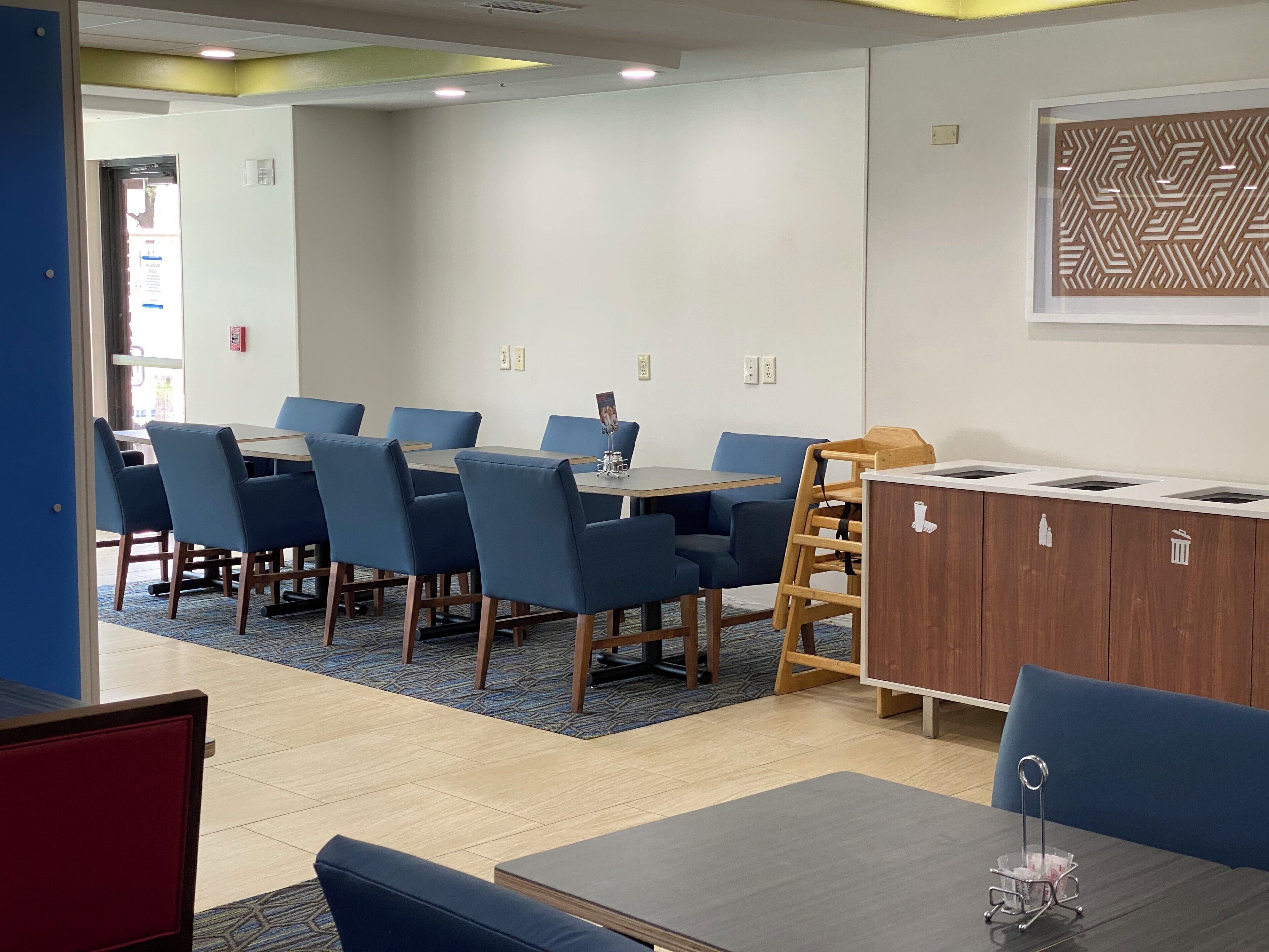 A conference room with a rectangular table, blue chairs, a wooden sideboard, and a patterned wall decoration.