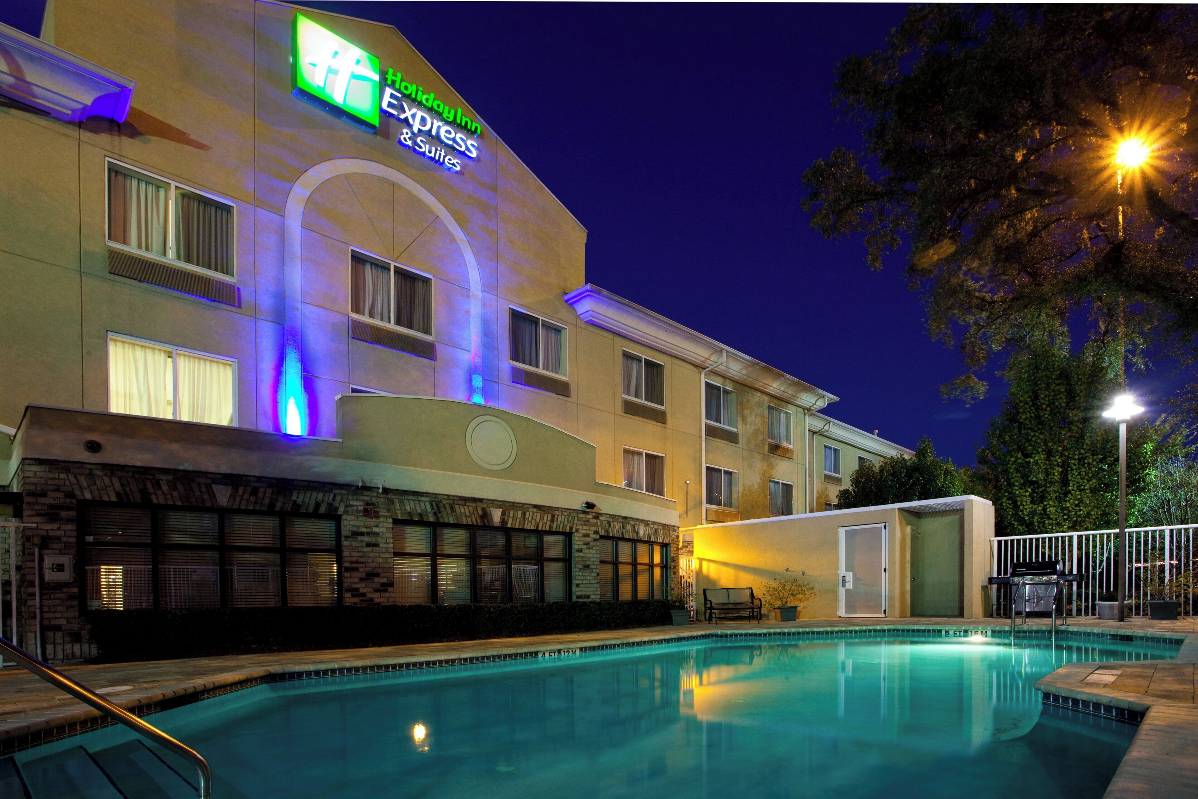 A Holiday Inn Express hotel with a swimming pool, outdoor seating, and a well-lit facade.