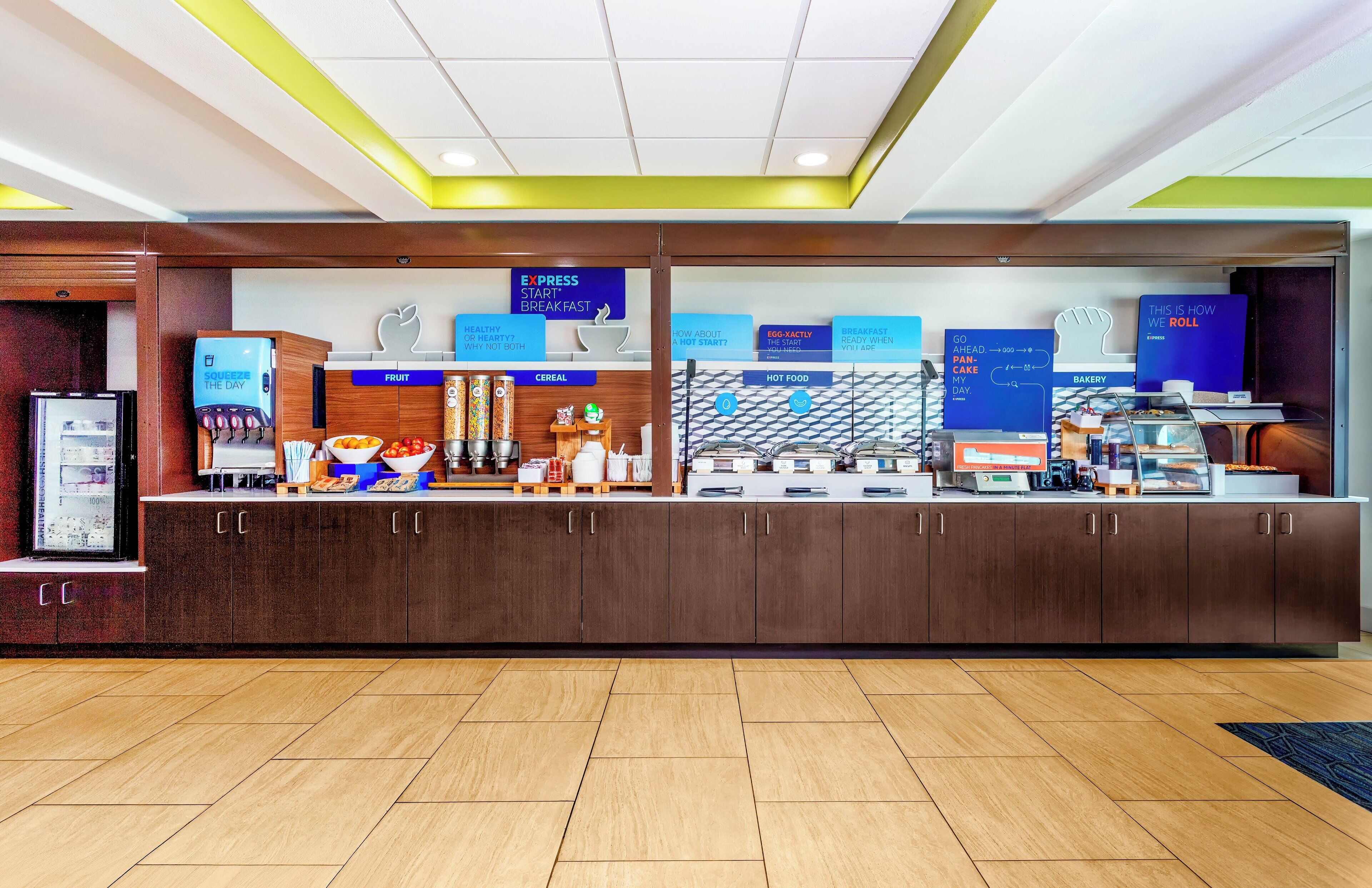 Zona de recepción de hotel con mostrador que muestra opciones de desayuno, una pantalla digital y una máquina de café.