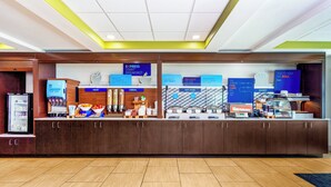 Un espace d’accueil d’hôtel avec un comptoir où sont présentés les différents choix de petit-déjeuner, un écran numérique et une machine à café.