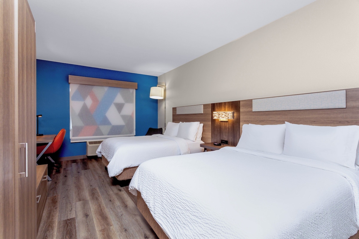 Quarto de hotel com duas camas, uma mesa e uma cadeira.