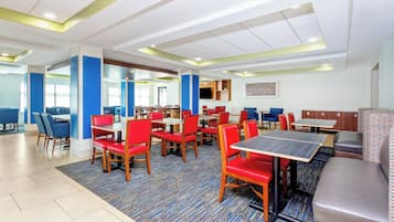 A hotel dining area with multiple tables and chairs, a patterned carpet, and a modern ceiling design.