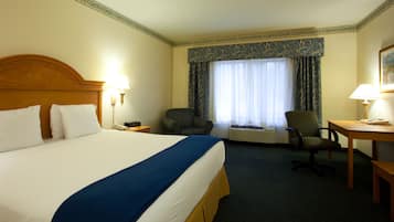 Una habitación de hotel con una cama grande, un escritorio, una silla y una ventana con cortinas.