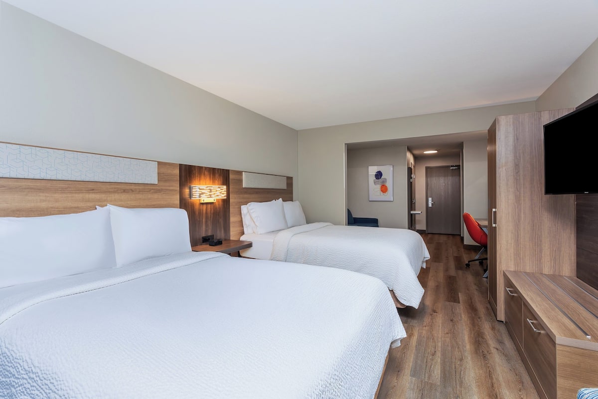 Ein Hotelzimmer mit zwei Betten, einem Fernseher, einem Schreibtisch und einem Stuhl.