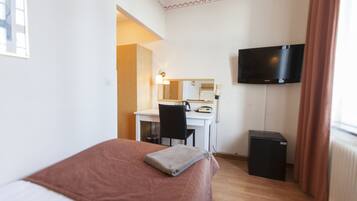 A hotel room with a bed, a desk, a chair, a television, and a small black cabinet.
