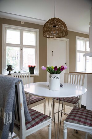 A dining area with a round table, checkered chairs, a hanging wicker light fixture, and a window with a view of the outside. - Eksjo Stadshotell (Eksjo)