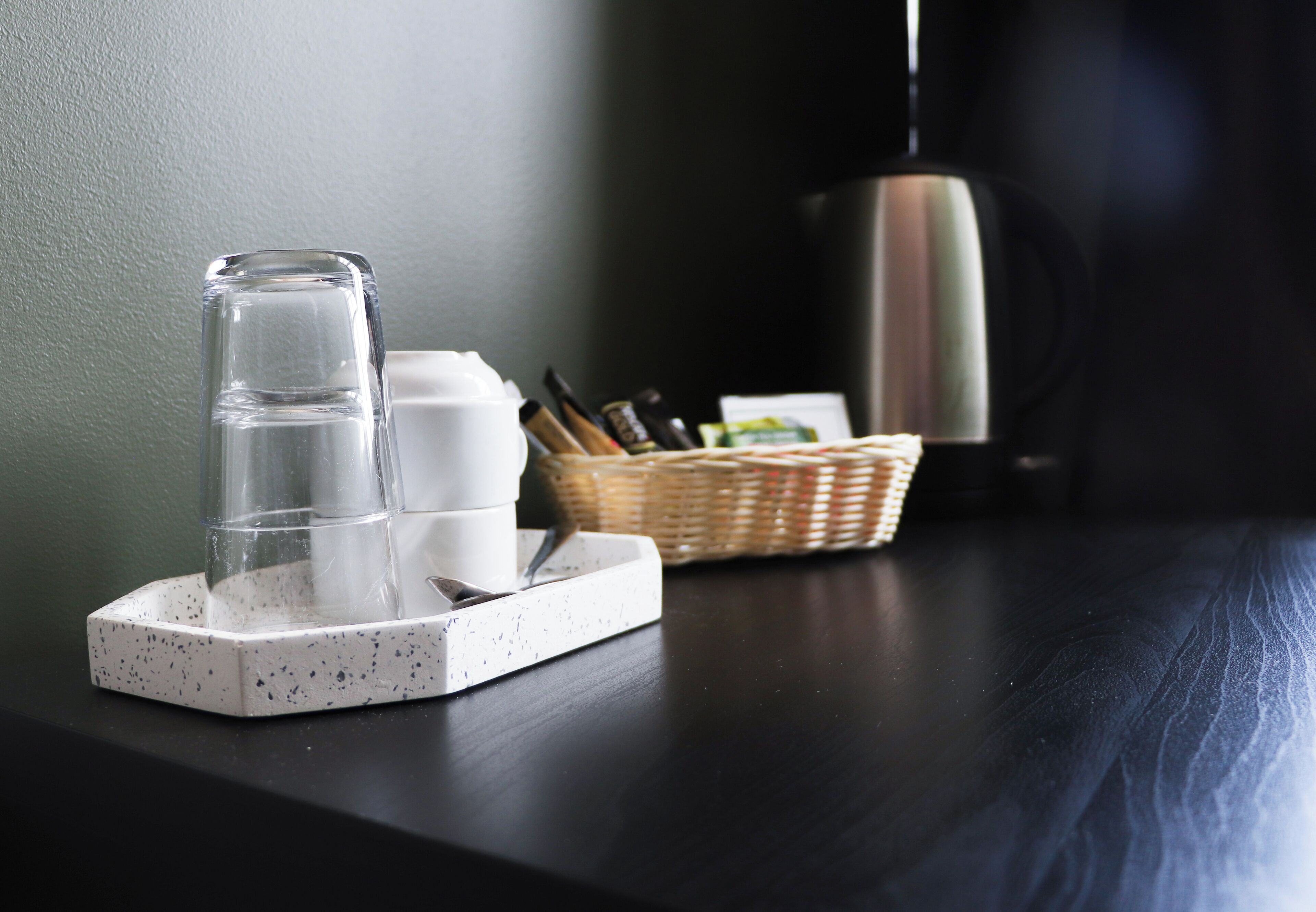 Et glas vand på en bakke, en kurv med penne, og en lampe på en mørk overflade.