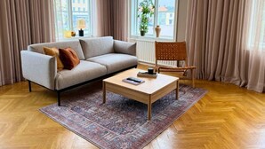 Una sala moderna con un sofá gris, una mesa de centro de madera y una alfombra estampada.