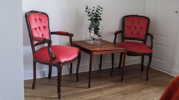 A dining area with two wooden chairs with red upholstery and a glass vase with a plant on a wooden table.