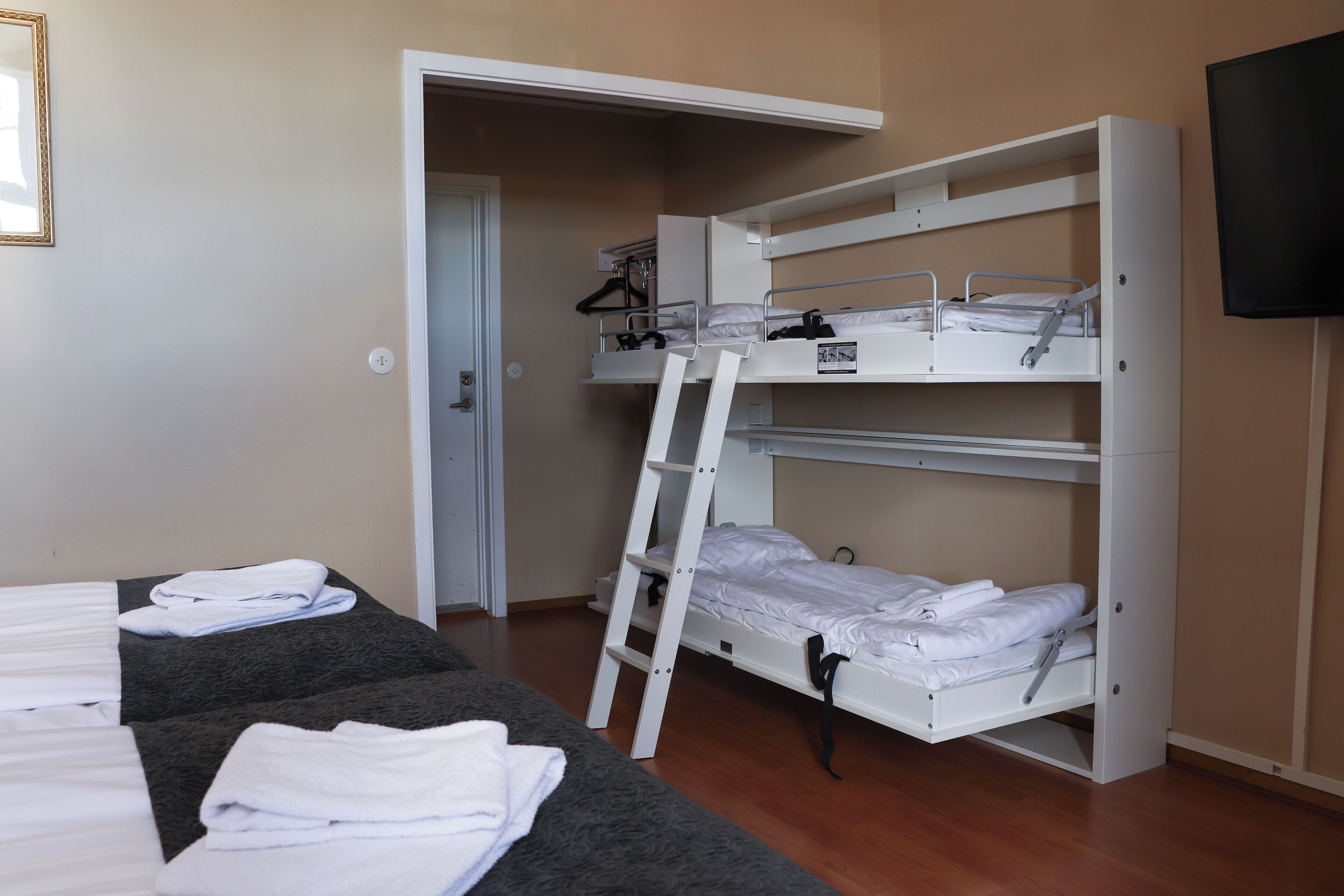 Ein Schlafzimmer mit Etagenbett und einer Leiter, einem flachen Bett mit Handtüchern, einem Fernseher und einer Tür zu einem weiteren Raum.