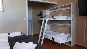 Ein Schlafzimmer mit Etagenbett und einer Leiter, einem flachen Bett mit Handtüchern, einem Fernseher und einer Tür zu einem weiteren Raum.