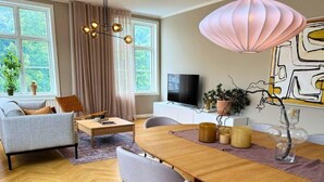 Una sala de estar moderna con una mesa de comedor de madera, sofás grises y un amplio ventanal con cortinas.
