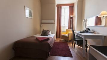 A hotel room with a bed, a desk, a chair, a lamp, and a window with curtains.
