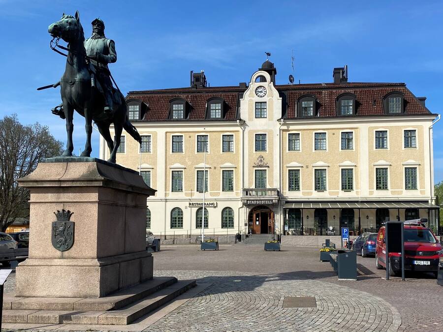 A statue of a mounted figure in front of a building with a clock tower, a restaurant, and a parking sign.