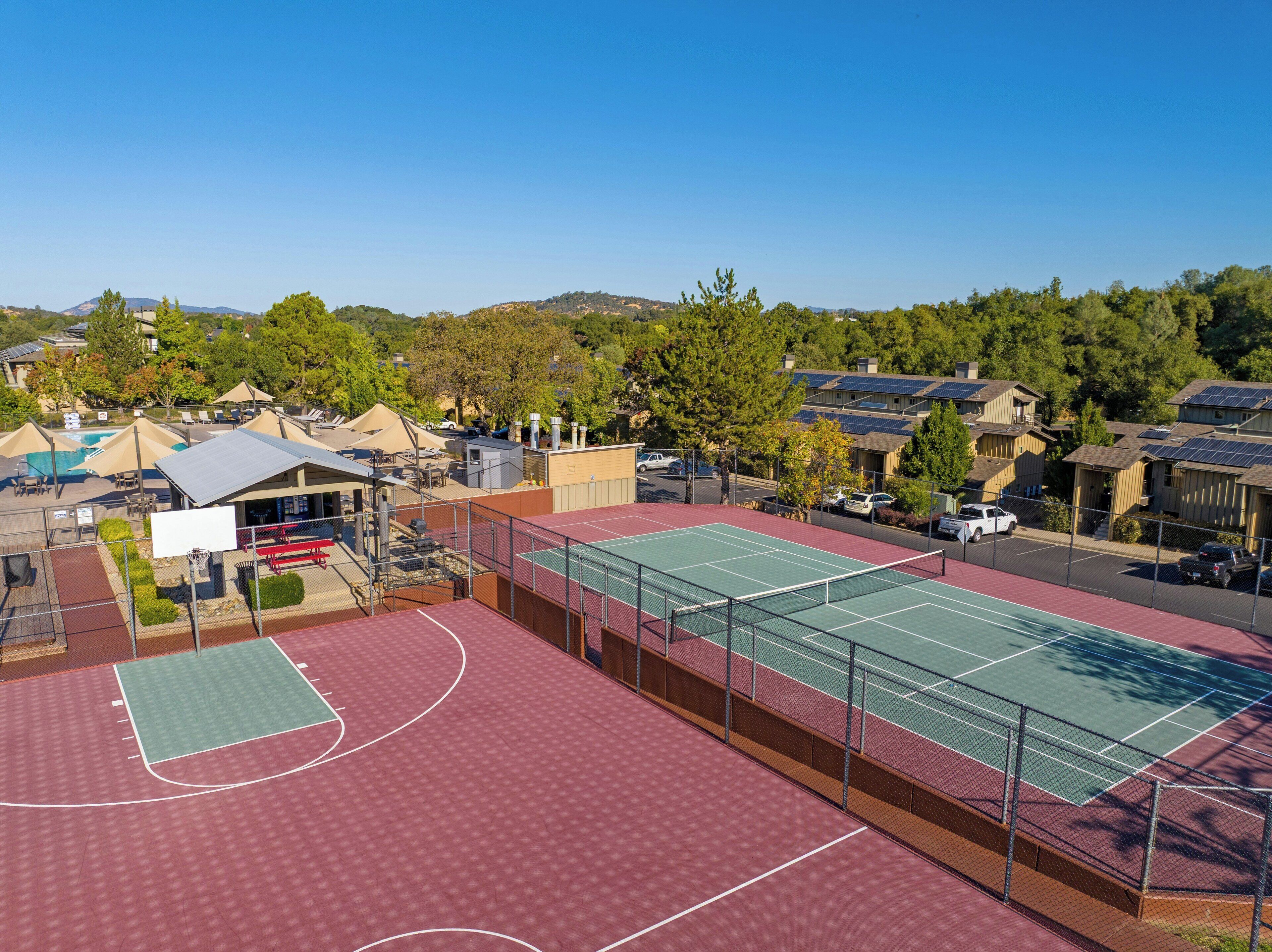 A sports complex with multiple tennis courts, a covered seating area, and a swimming pool.