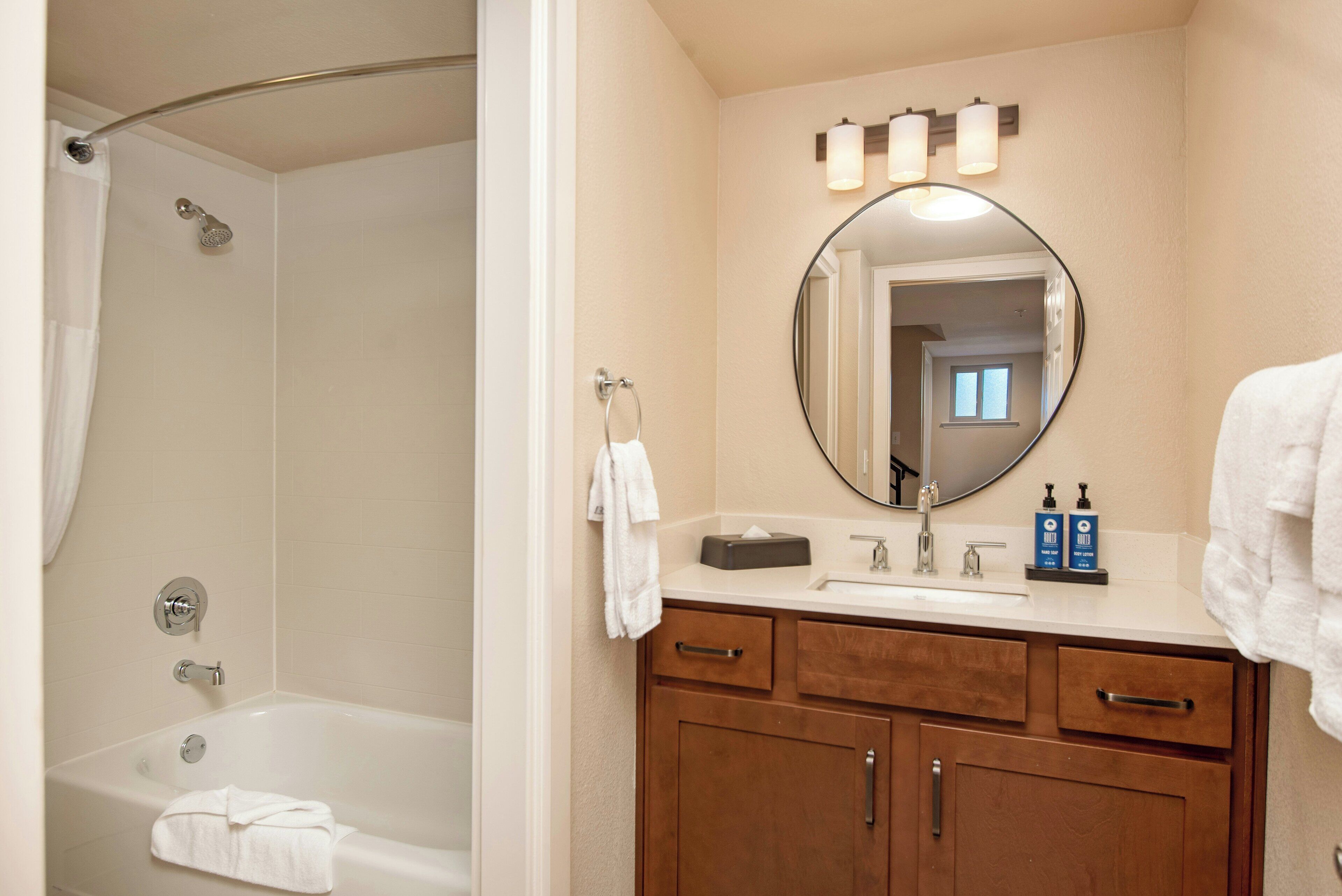 A bathroom with a bathtub, a sink, a mirror, and wooden cabinets.