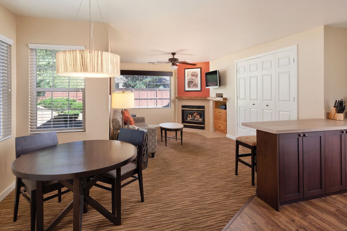 A modern kitchen with a fireplace, dining area, and a ceiling fan.