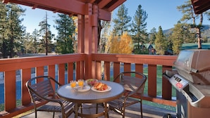 A covered outdoor area with a round table, two chairs, a grill, and a view of trees and houses in the background. - WorldMark Big Bear Lake (Big Bear Lake)