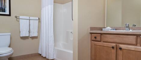 A bathroom with a toilet, a shower with a curtain, a sink with a mirror, and wooden cabinets.